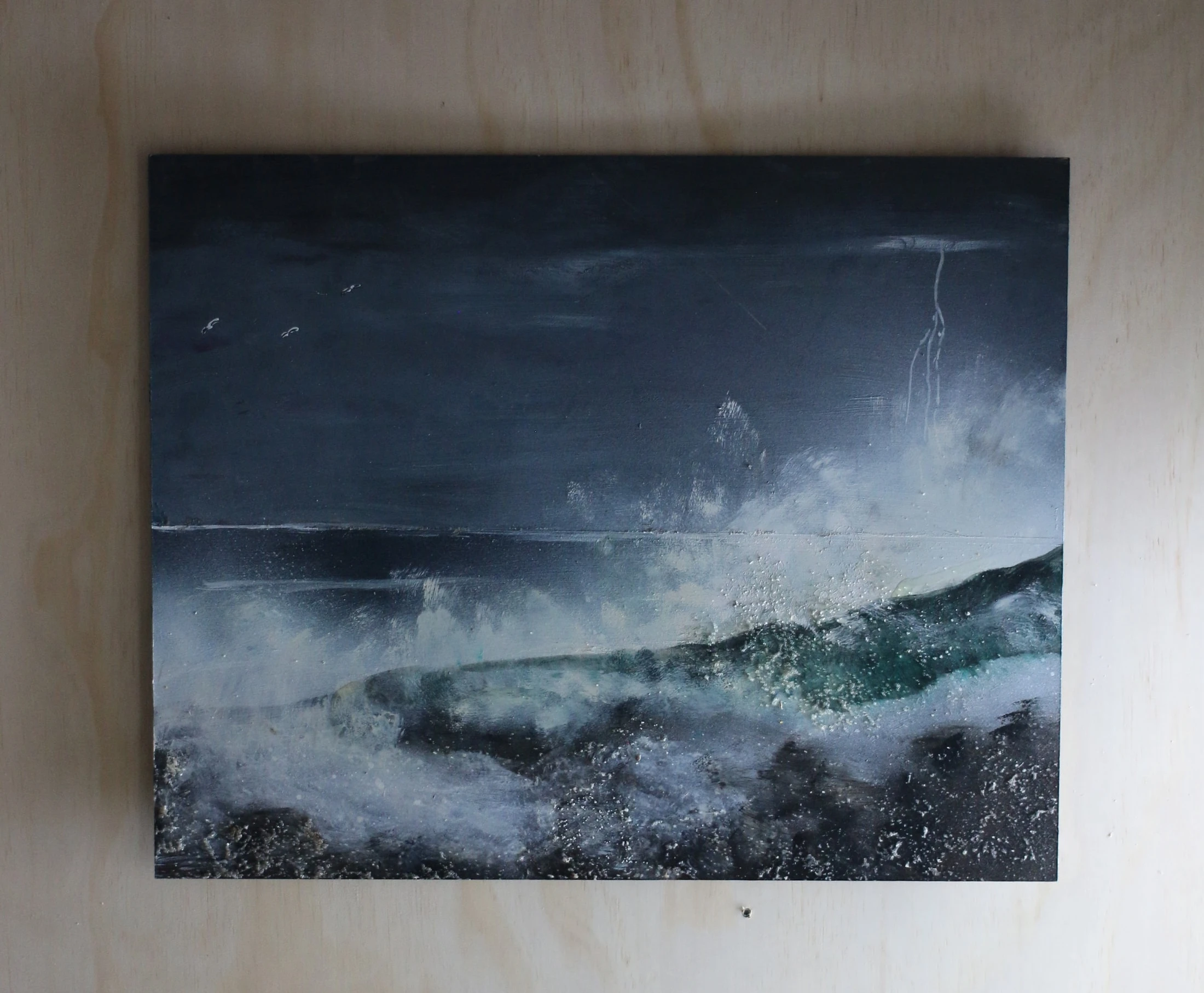 Another photograph of the same waves and lightning painting, shown without a frame against a wall.