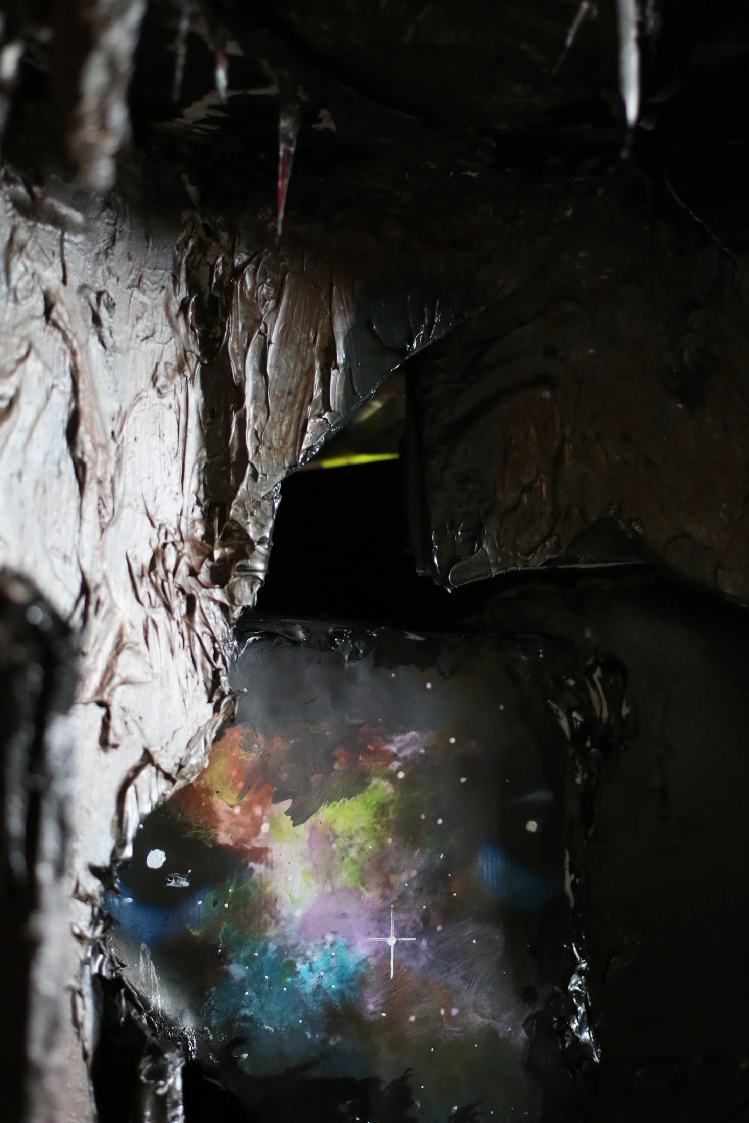 A colourful patch of stars seen through a dark, textured opening in a studio piece.