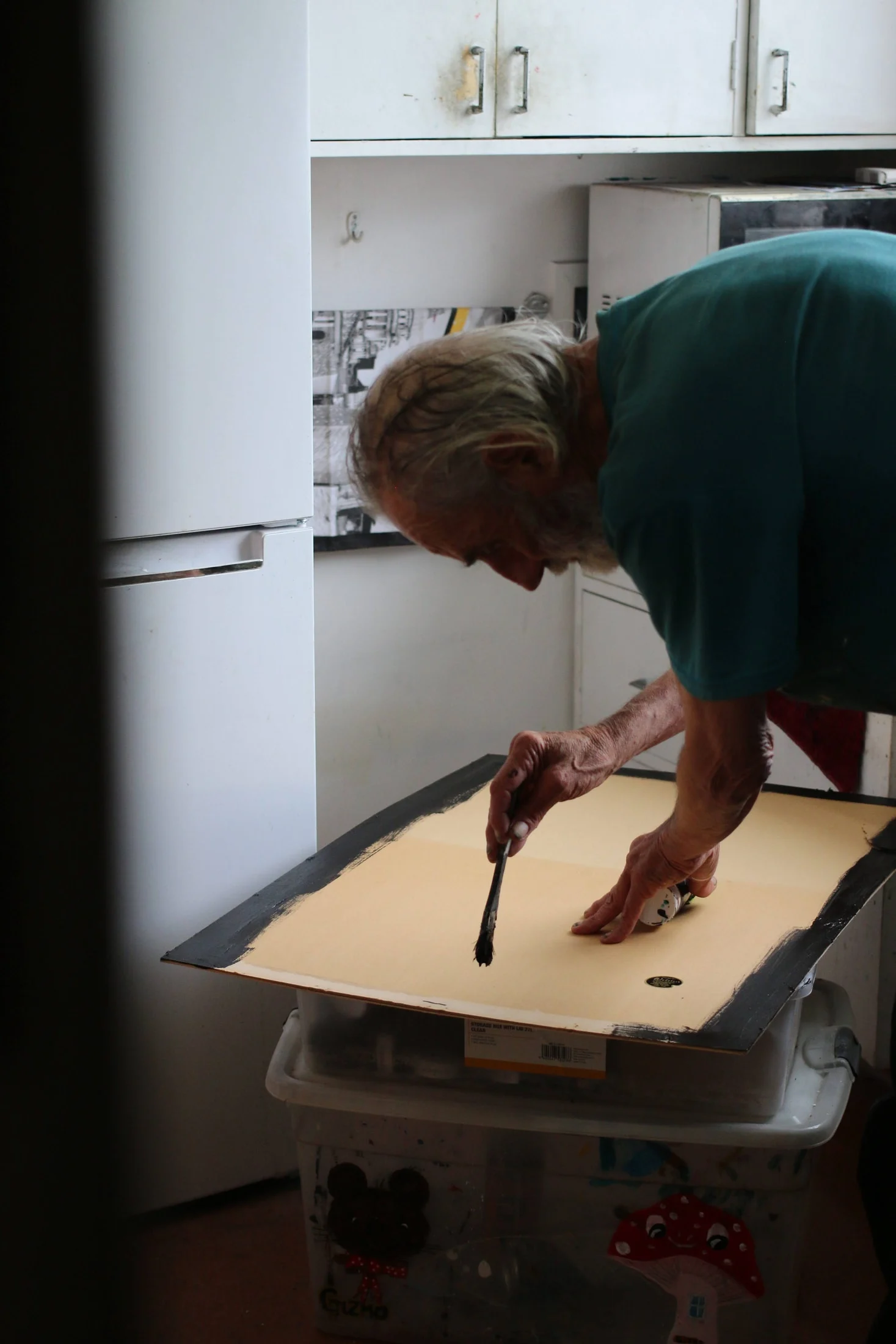 John leaning over a board and painting at a small table in the kitchen.